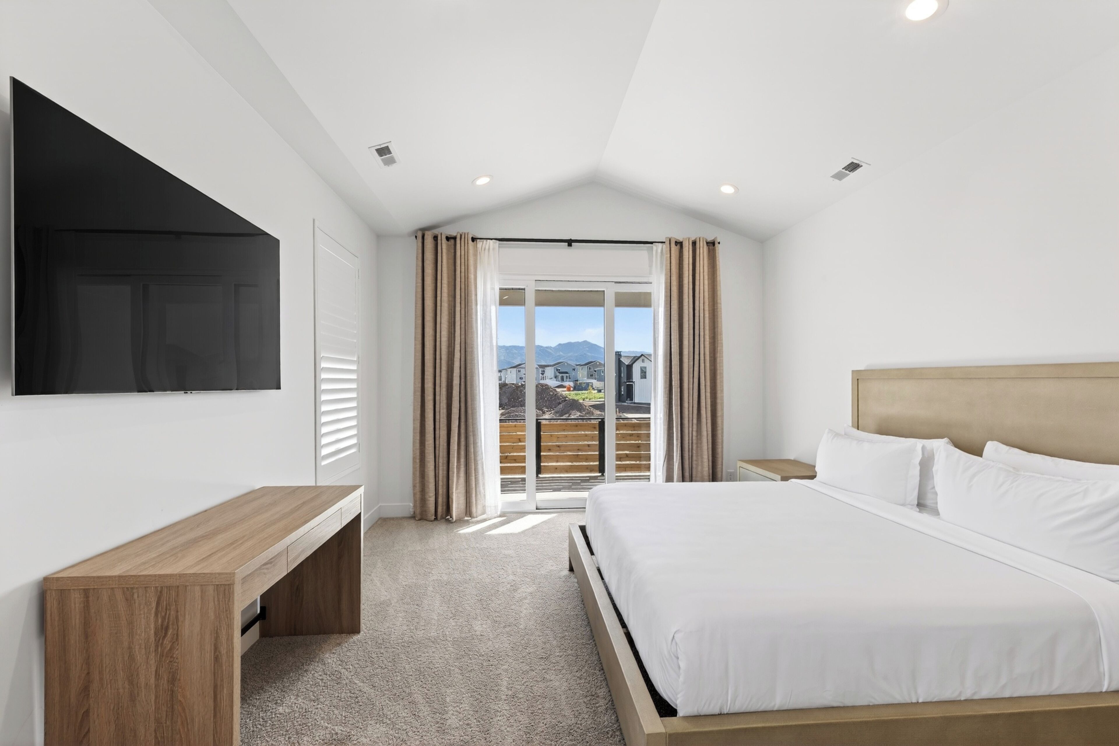 A bedroom with a bed, a TV, a desk, and a sliding door to a balcony.