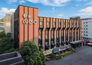 Un hotel moderno con un cartello ben visibile, diversi piani e un cortile con posti a sedere all'aperto.