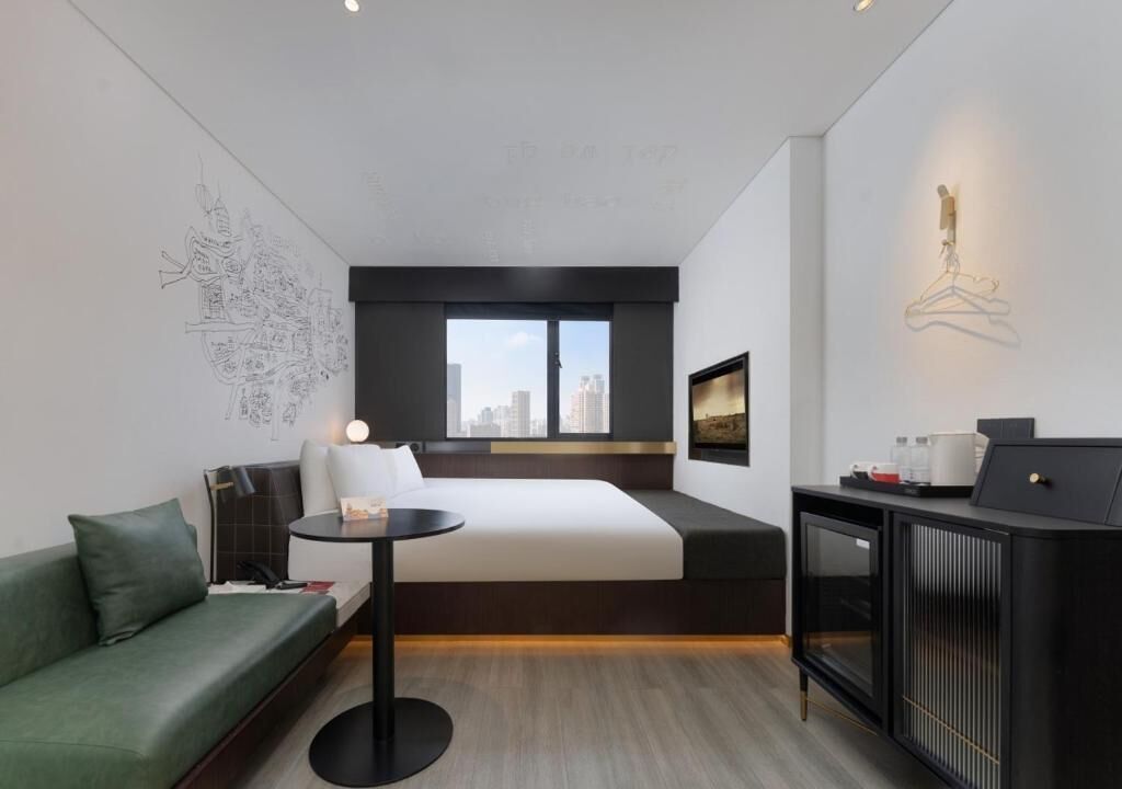 Una moderna camera d'albergo con un letto, un divano verde, un tavolino, un armadietto e vista sulla città.