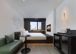 A modern hotel room with a bed, a green sofa, a small table, a cabinet, and a cityscape view.
