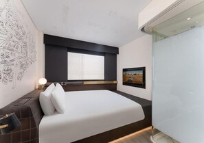 A modern hotel room with a large bed, a window, a wall-mounted TV, and a wall art piece.