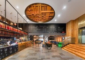 A modern bar area with a digital flight information display, a wooden accent wall, and a seating area with a vintage cart.