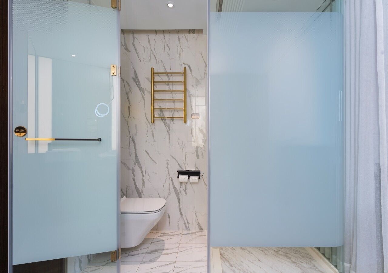 A modern bathroom with a glass partition, a marble wall, a toilet, and a towel rack.
