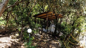 A covered wooden structure with steps leading to a stone wall, surrounded by dense foliage. - Casa Orizzonte-Vista Sul Mare Del Circeo (Punta Rossa)
