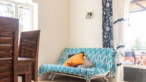 A room with a wooden chair, a patterned sofa, a small wall-mounted light, and a window with curtains. - Casa Orizzonte-Vista Sul Mare Del Circeo (Punta Rossa)