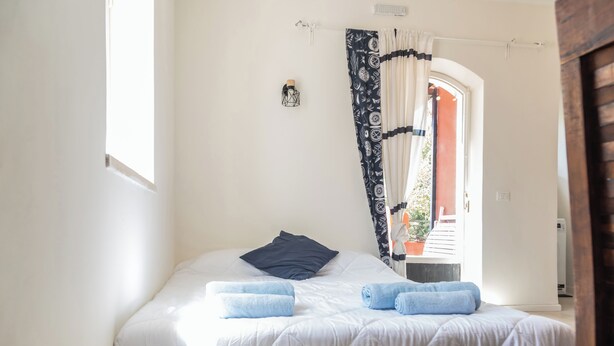 A bed with white bedding, two rolled towels, a dark pillow, and a patterned curtain. - Casa Orizzonte-Vista Sul Mare Del Circeo (Punta Rossa)
