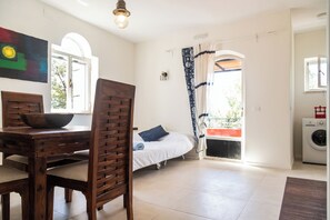 Ein Zimmer mit einem Bett, einem Tisch mit einer Schüssel, einem Stuhl, einer Waschmaschine und einem Fenster mit Vorhängen.
