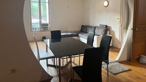 Ein Zimmer mit Esstisch, Stühlen, einer Couch, einem Fenster und einer Tür.