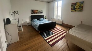 Ein Schlafzimmer mit Bett, Schreibtisch, Stuhl, Heizkörper, Fenster und einem Bild an der Wand.