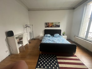 Een slaapkamer met een bed, bureau, radiator en raam.
