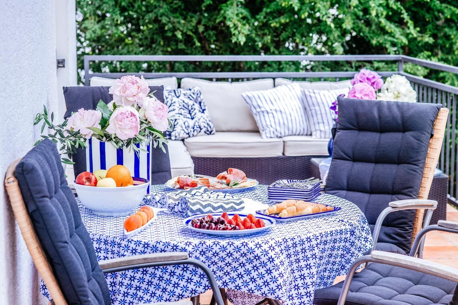 An outdoor dining area with a table set for a meal, surrounded by chairs and a sofa.