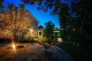 A house with a stone patio, outdoor seating, and a car parked nearby.