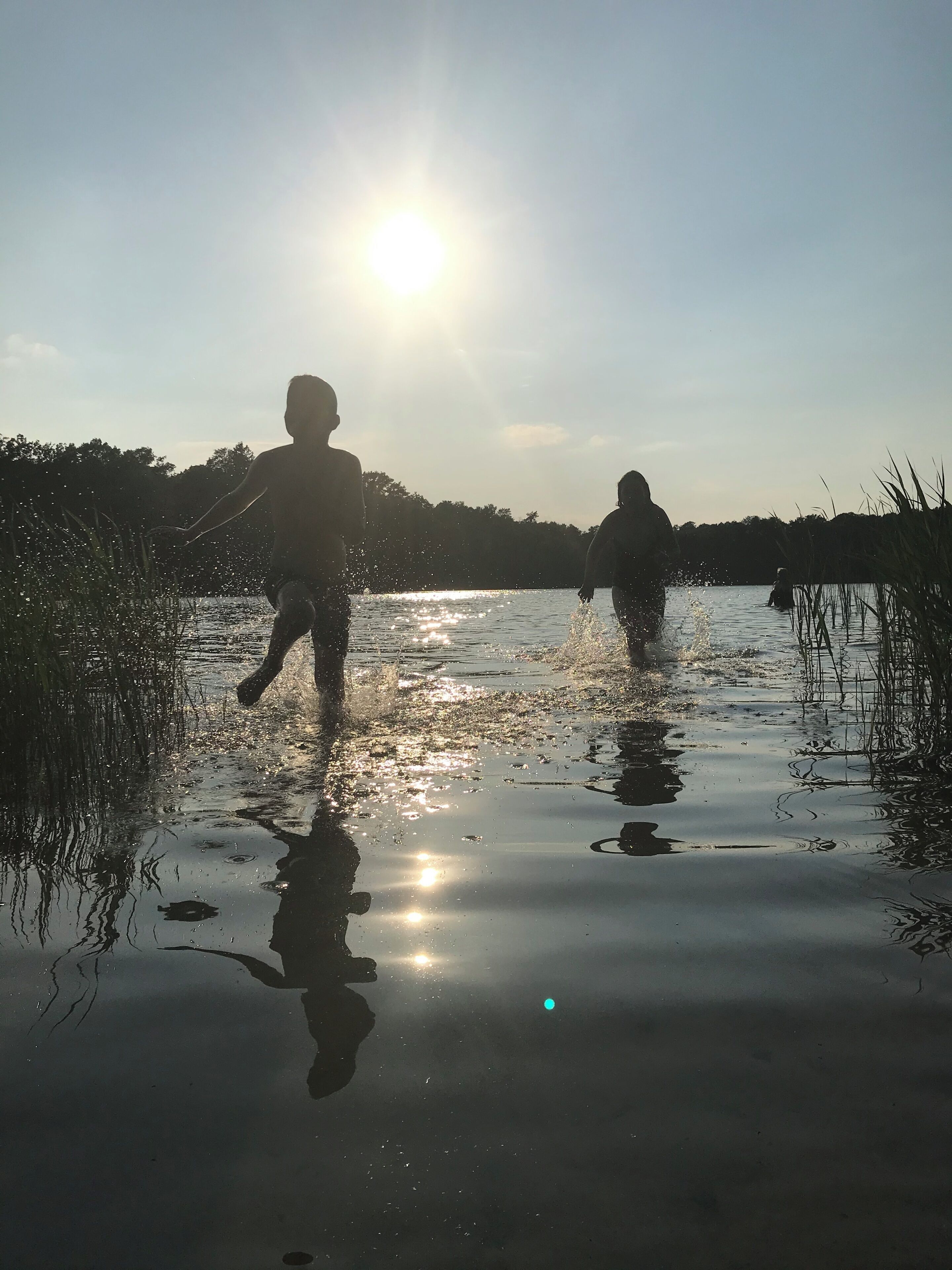 A body of water with reflections of the sun and silhouettes of people.