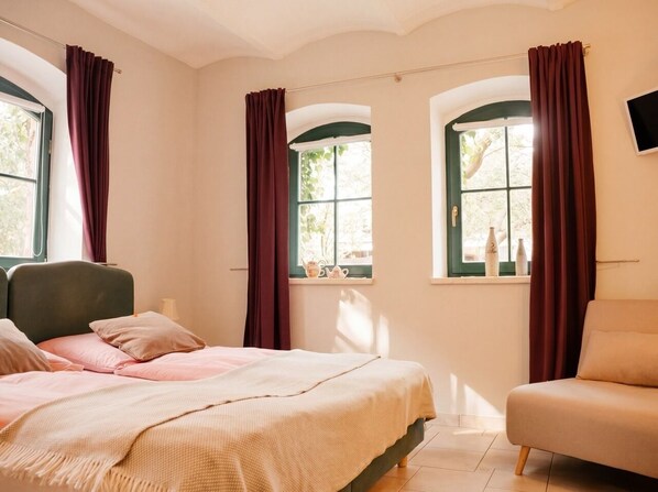 Ein Schlafzimmer mit einem Bett, einem Sessel und zwei mit Vorhängen versehenen Fenstern.