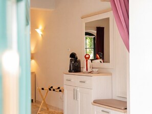 Ein Zimmer mit einer Küchenzeile, einem Spiegel, einer Kaffeemaschine und einem fenster mit Vorhängen.
