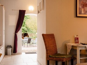 Ein Zimmer mit Stuhl, Tisch mit einem Buch, Mülleimer und Blick auf einen Außenbereich mit Tisch und Stühlen.