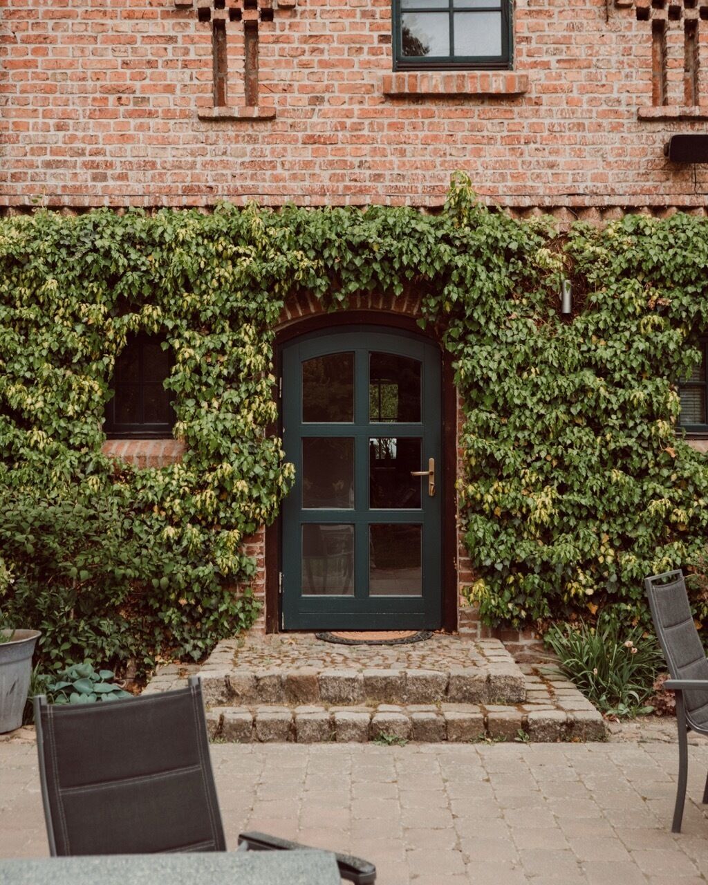 Un bâtiment en briques avec une porte verte et des murs couverts de lierre.
