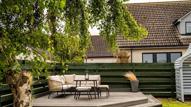 Une terrasse avec des meubles d’extérieur, une plateforme en bois et une maison en arrière-plan.