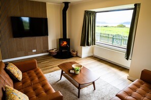 A living room with a television, a fireplace, a sofa, and a view of the outdoors. - Cozy Highland Cottage Escape (Inverness)