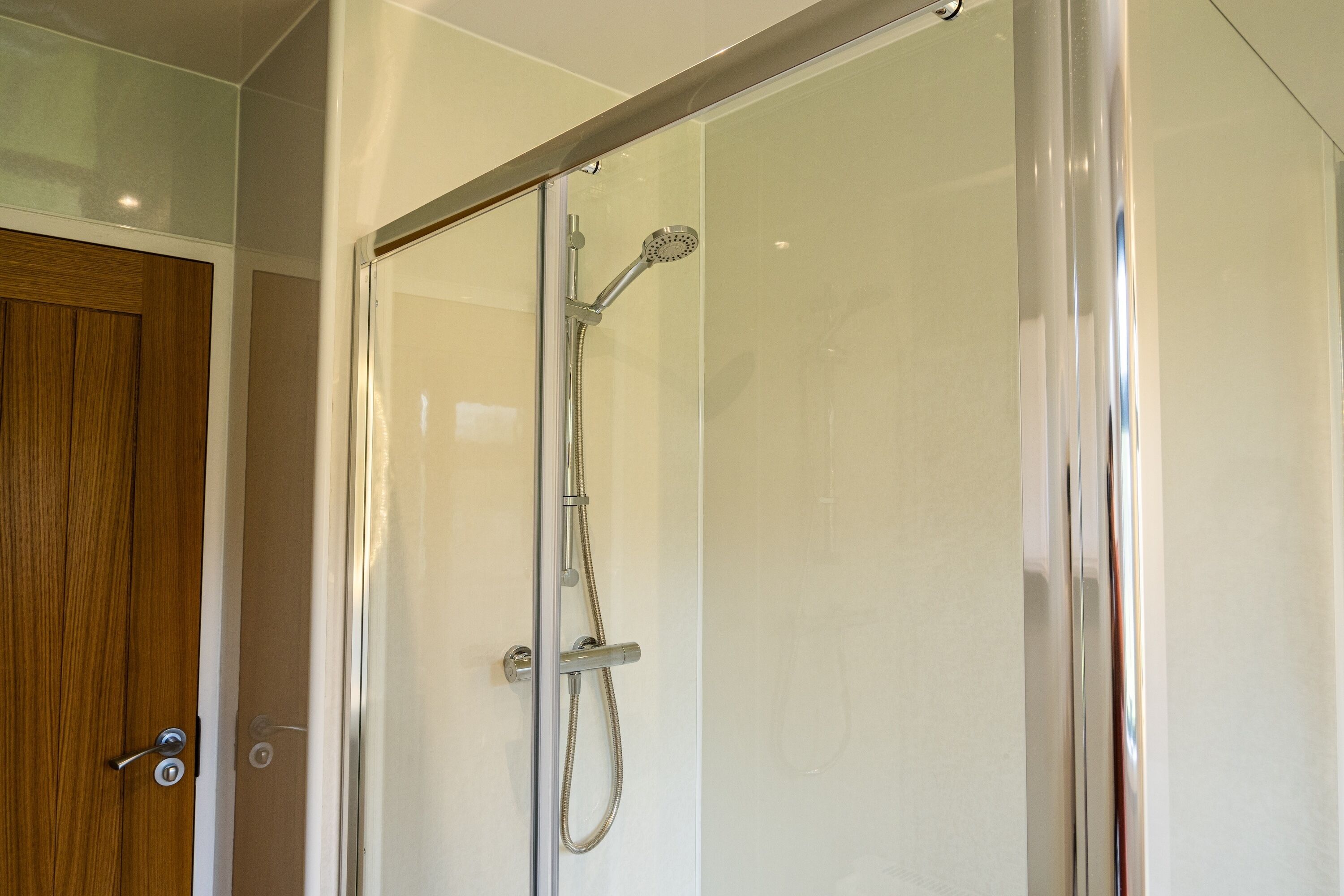 A glass-enclosed shower with a handheld showerhead and a wall-mounted faucet.