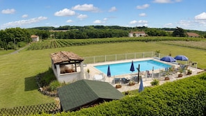 Ein Pool mit umzäunter Liegefläche, umgeben von üppigem Grün und blauem Himmel.