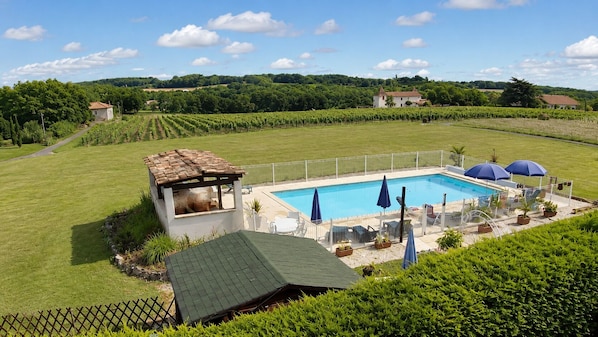 Une piscine dotée d’une terrasse entourée de clôtures, bordée d’une végétation luxuriante et surplombée par un ciel dégagé.