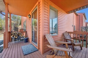 En træterrasse med to Adirondack-stole, et brændeskur og en dør, der fører til en overdækket veranda.