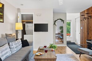 En moderne stue med sofa, sofabord med mad og drikkevarer, et fjernsyn ophængt på væggen og en trævægsbeklædning.