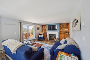 Ein Wohnzimmer mit blauen Sofas, einem Kamin, einem Fernseher und einem Bücherregal.