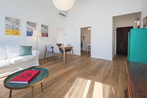 A modern living room with a white sofa, a glass coffee table with a book, a dining area with a table and chairs, and a kitchen in the background. - Apartments Florence -Blue Shade over Florence (Firenze)