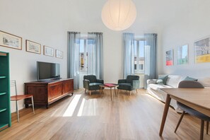Un soggiorno moderno con una TV a schermo piatto, due poltrone, un tavolo da pranzo in legno e un divano.