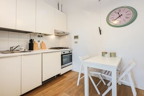 A modern kitchen with white cabinets, a stove, oven, and a dining area with a table and chairs. - Apartments Florence -Blue Shade over Florence (Firenze)