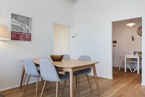 Zona pranzo con tavolo in legno e quattro sedie, una lampada a parete e una porta che conduce in un'altra stanza.