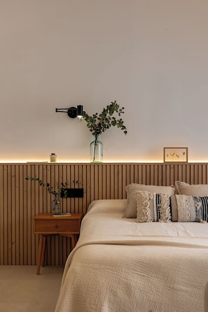 Et soveværelse med seng, natbord, lampe, vase og et billede på væggen.