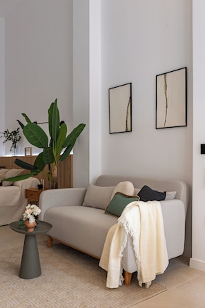 En stue med sofa, sofabord, en plante og kunst på væggen.