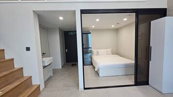 A modern hotel room with a bed, a bathroom with a sink, and a staircase.
