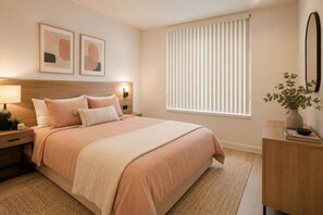 Ein Schlafzimmer mit Bett, Nachttischen, einer Nachttischlampe, einem wandmontierten Spiegel, einem Fenster mit Jalousien und zwei gerahmten abstrakten Kunstwerken.