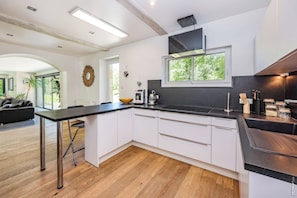 A modern kitchen with a black countertop, white cabinets, and a large window. - House in Bouyssou - Nature and Elegant (Viterbe)