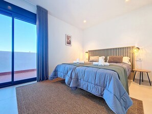 A hotel room with a large bed, a small table, a wall-mounted lamp, and a view through a large window. - Penthouse | Private Terrace & Pool Views (Los Alcazares)
