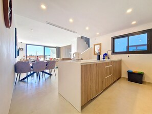 A modern kitchen with a central island, dining area with chairs, and a large window. - Penthouse | Private Terrace & Pool Views (Los Alcazares)