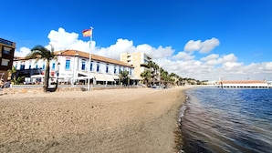 Un hotel frente a la playa con arena, palmeras y una bandera.
