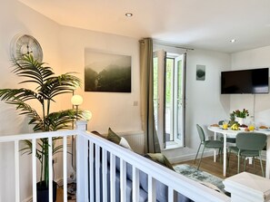 Uma sala de estar moderna com escada, área de jantar com mesa e cadeiras, televisão e uma janela grande com cortinas.