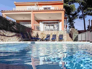 A hotel with a swimming pool, lounge chairs, and a stone facade. - Chalet Mirador in Alcudia - Puerto de Alcudia (Alcúdia)
