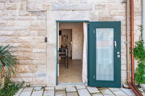 A stone building with a green door, a small room with a chair and table, and a potted plant. - La Chicca Sul Mare Sea View (Bisceglie)