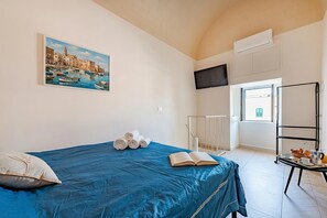 Una stanza con un letto, un quadro, una TV, un termosifone, una finestra e un vassoio con prodotti per la colazione.