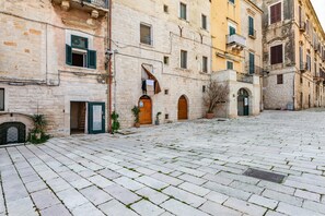A courtyard with stone paving, a building with a wooden door, and a balcony. - La Chicca Sul Mare Sea View (Bisceglie)