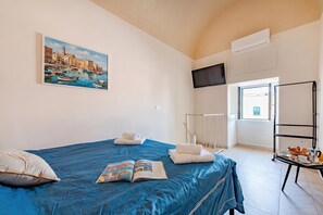 A hotel room with a bed, a painting of a coastal scene, a TV, and a breakfast trolley. - La Chicca Sul Mare Sea View (Bisceglie)