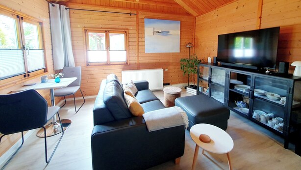 Un interior de cabaña acogedor, con sofá, televisor, mesa de comedor y una ventana con cortinas.
