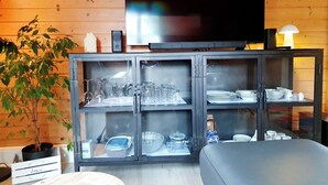 Una sala de estar con pared de madera, televisor, aparador con puertas de cristal y una planta.