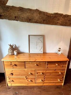 A wooden dresser with drawers, a framed abstract artwork, a pineapple, and a small bottle.